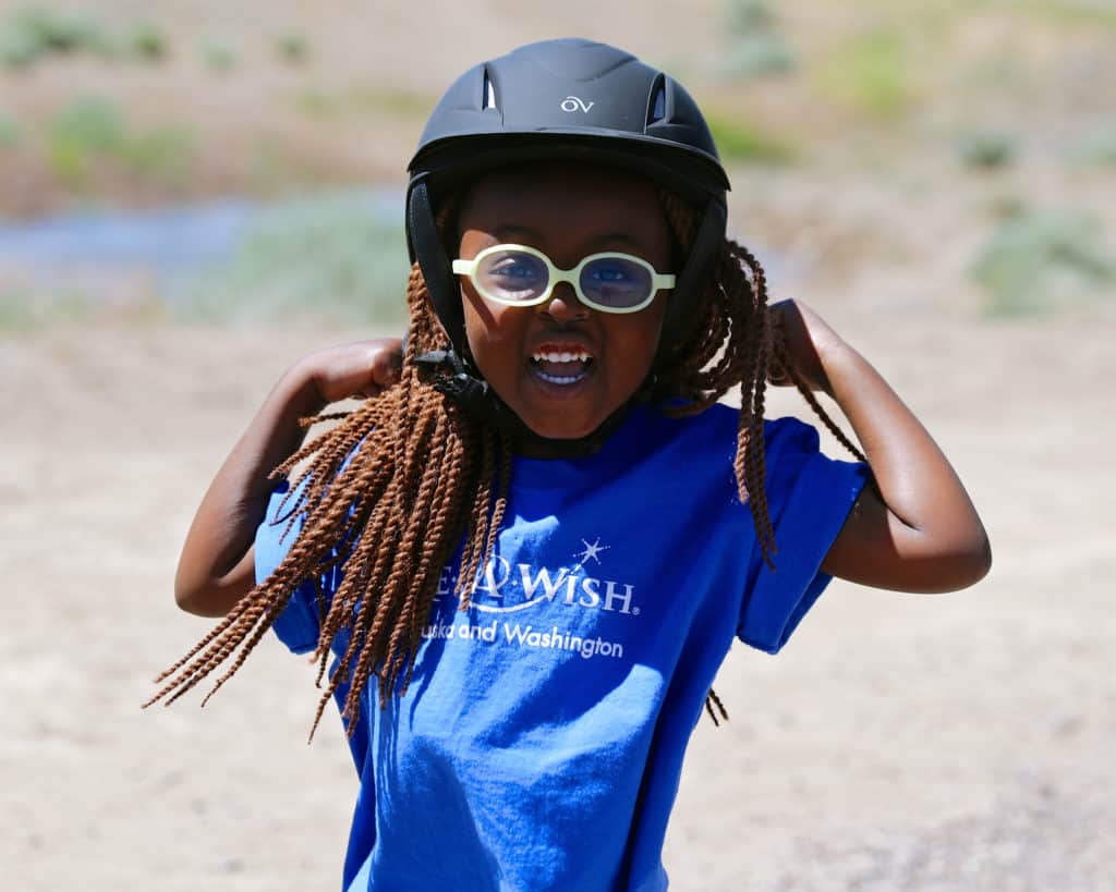 Make-A-Wish kid, Carmel, smiling with a helmet and goggles for horse riding